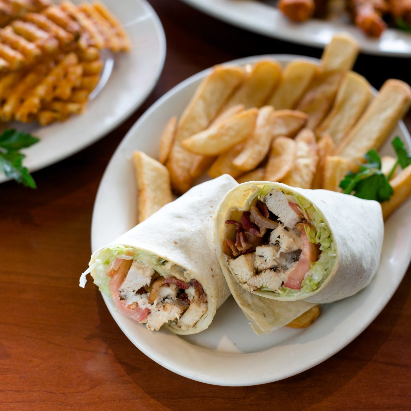 A plate of french fries and a chicken wrap on a table.